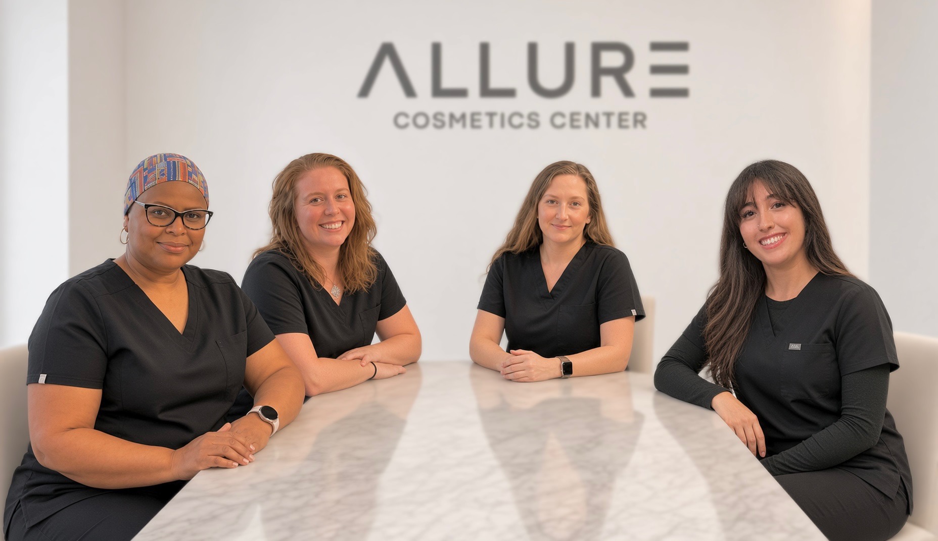 The Allure Cosmetics Center team in black scrubs smiling together at a marble table in front of the Allure Cosmetics Center logo in Southern Maryland